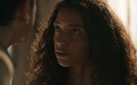 Alice Carvalho caracterizada como Joana; ela encara Irandhir Santos --de costas para a câmera-- em cena de Renascer