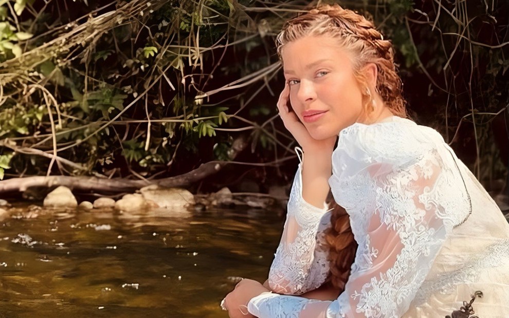Grazi Massafera usa uma trança e vestido branco na beira de um rio nas gravações de Dona Beja